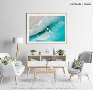 Girl walking back to shore with surfboard in blue water and waves in a natural fine art frame