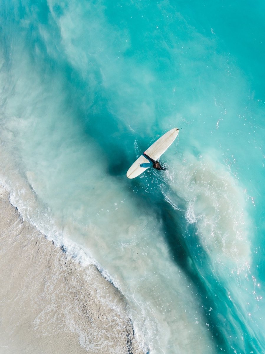 Girl walking back to shore with surfboard in blue water and waves