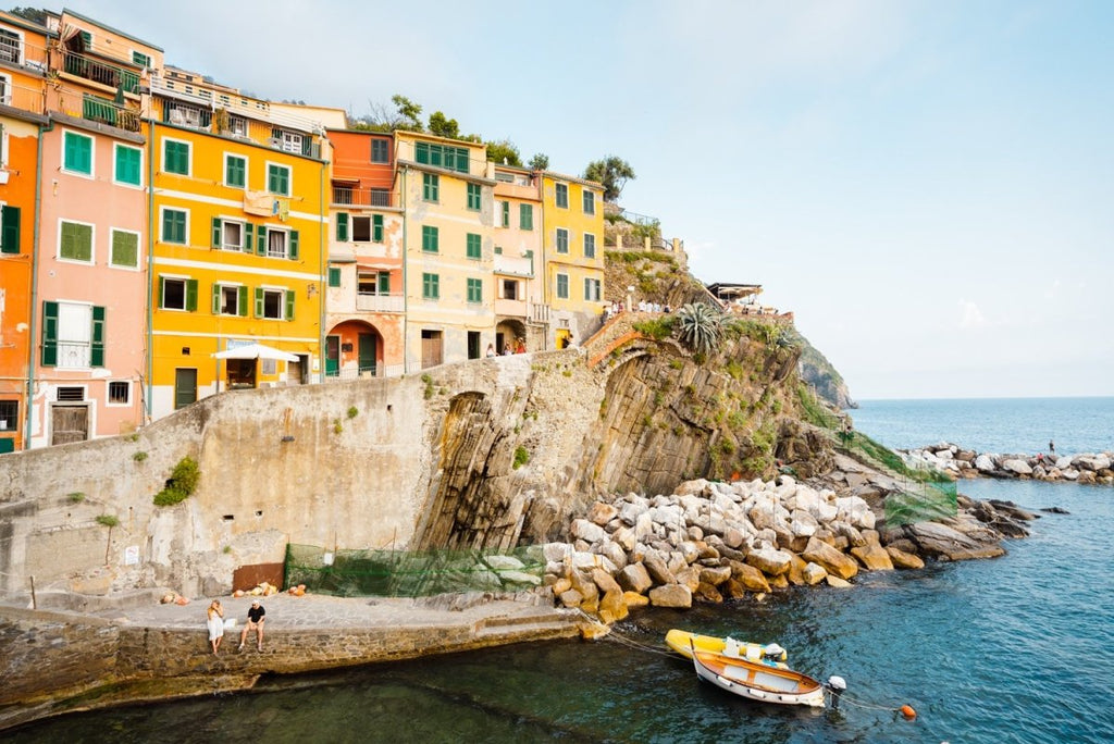 Man and woman sitting alongside docked boats and colorful buildings in Riomaggiore