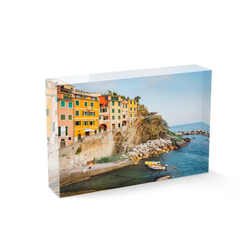 Man and woman sitting alongside docked boats and colorful buildings in Riomaggiore