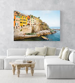 Man and woman sitting alongside docked boats and colorful buildings in Riomaggiore in an acrylic/perspex frame