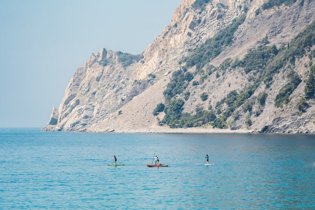Four people paddling on board alongside mountains in Cinque Terre