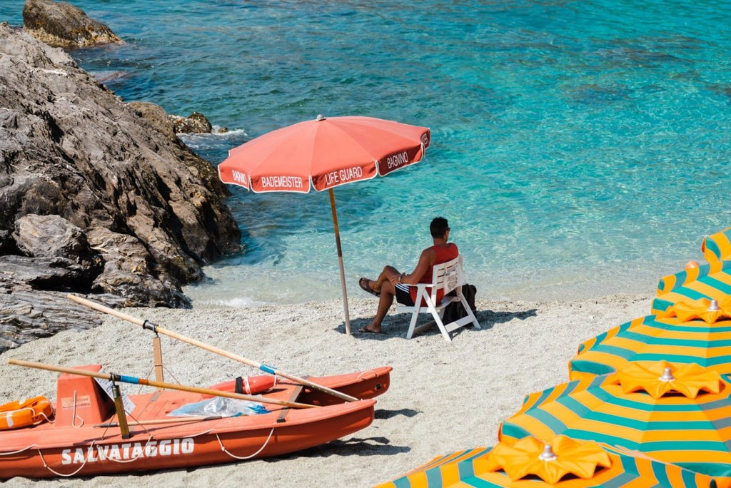Italian lifeguard sitting under umbrella at blue water on Monterosso Beach