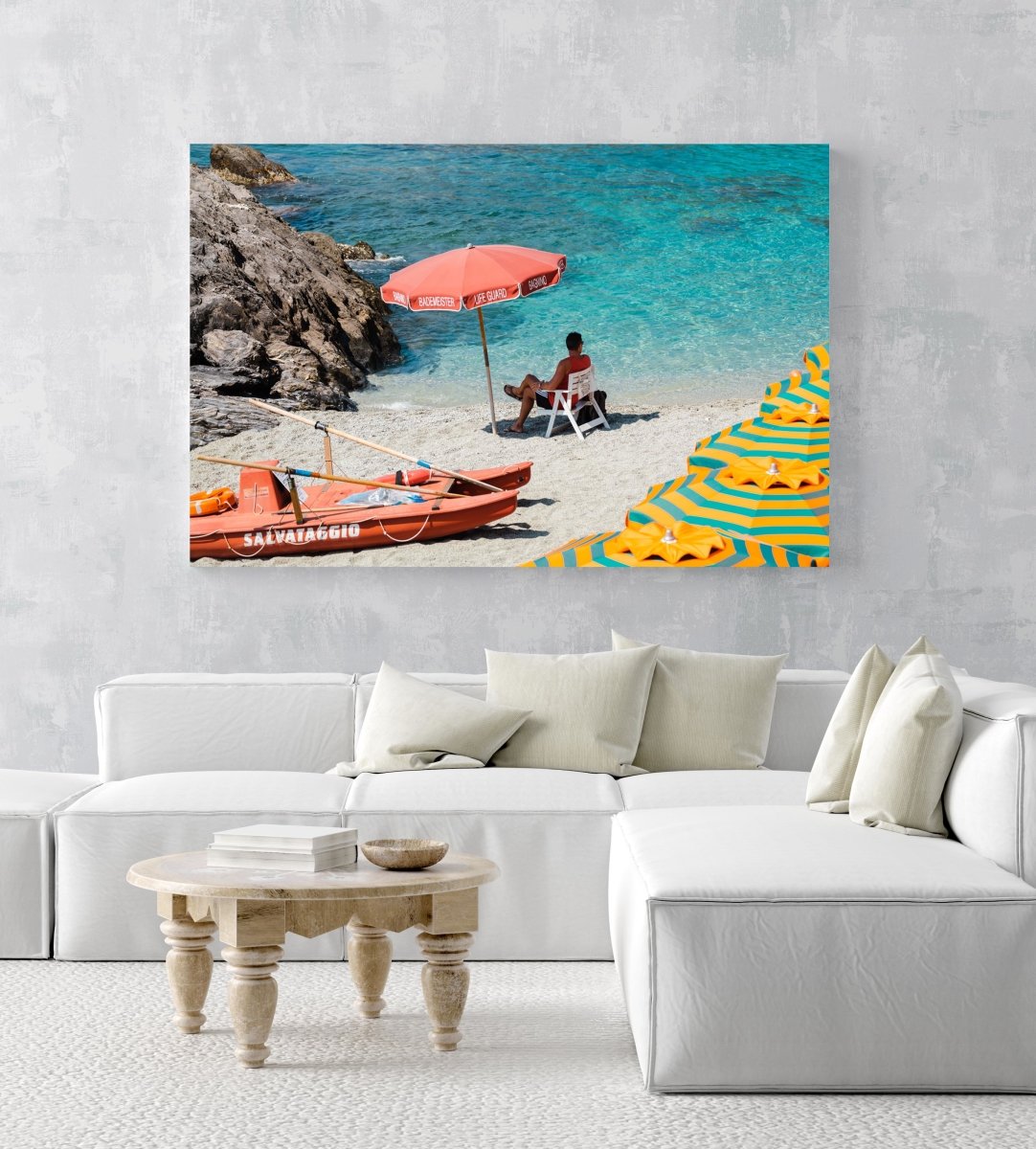 Italian lifeguard sitting under umbrella at blue water on Monterosso Beach in an acrylic/perspex frame