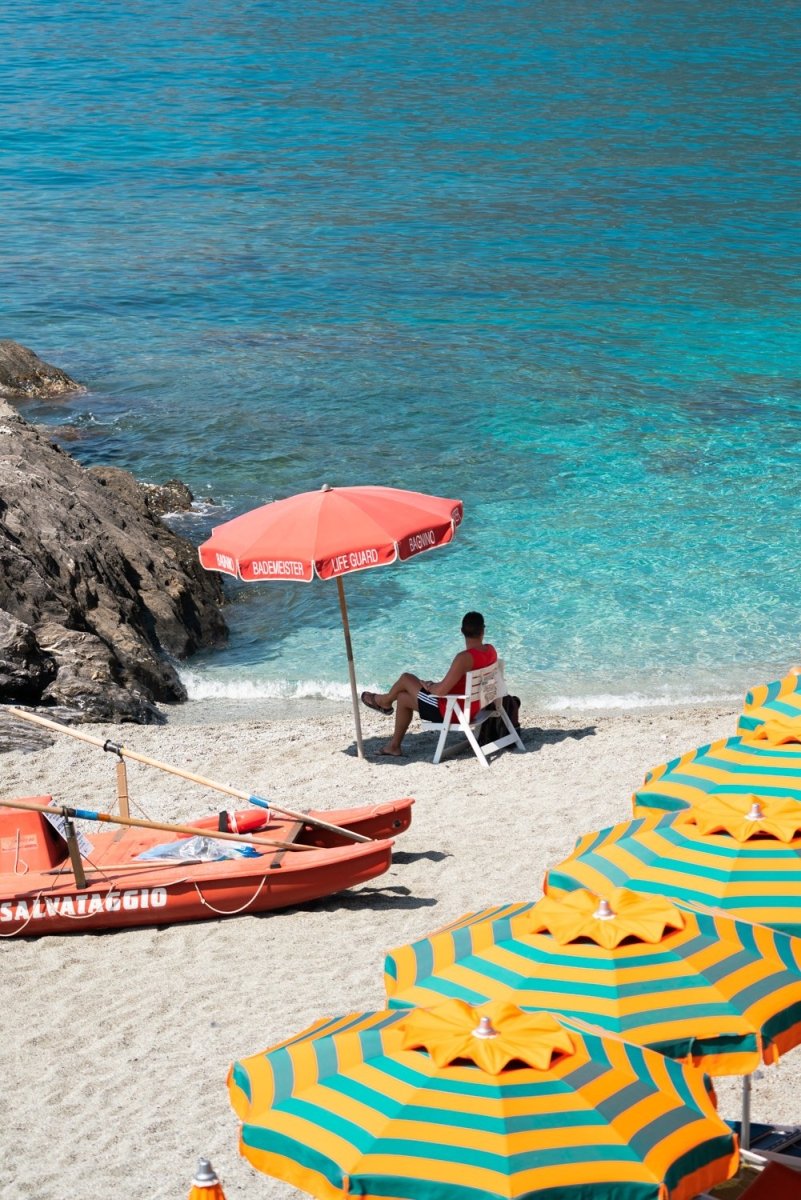Italian lifeguard sitting under umbrella with boat at blue water on Monterosso Beach