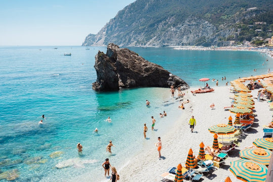 Big rock on Monterosso beach surrounded by people and blue water Cinque Terre