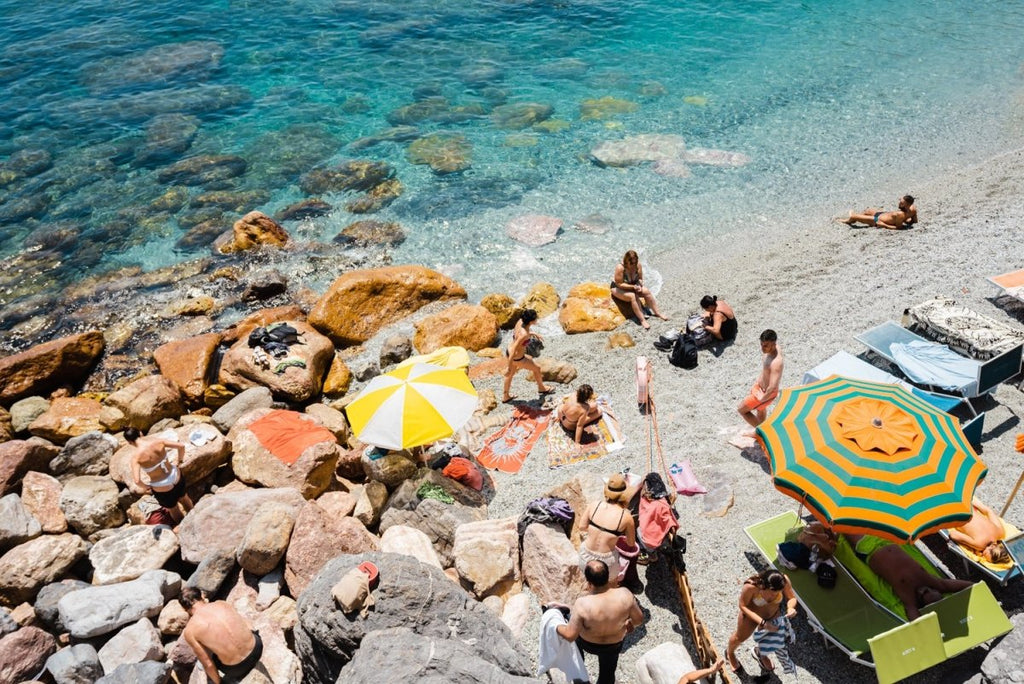 Umbrellas and people on beach with rocks and sand in Cinque Terre