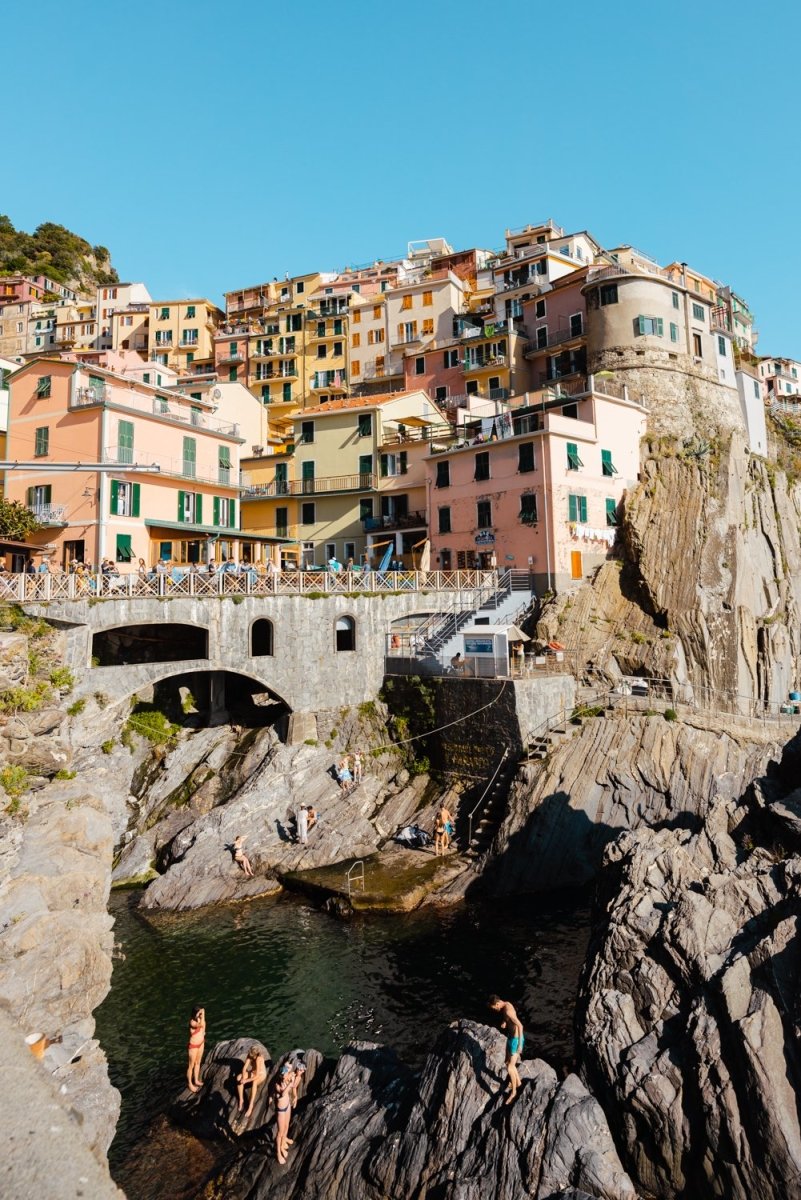 People swimming amongst bridge and colorful buildings of Manarola in Cinque Terre