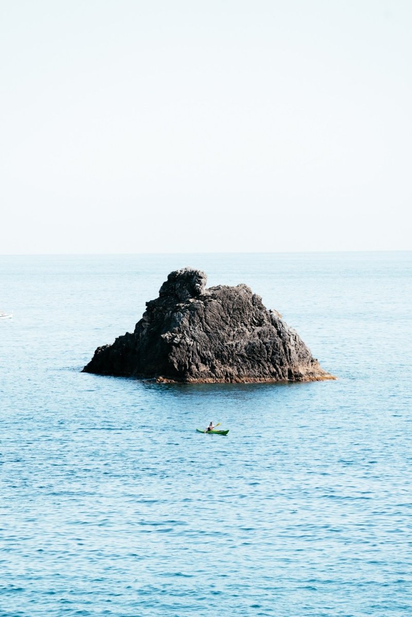 Man paddling in kayak at big rock in blue ocean in Cinque Terre