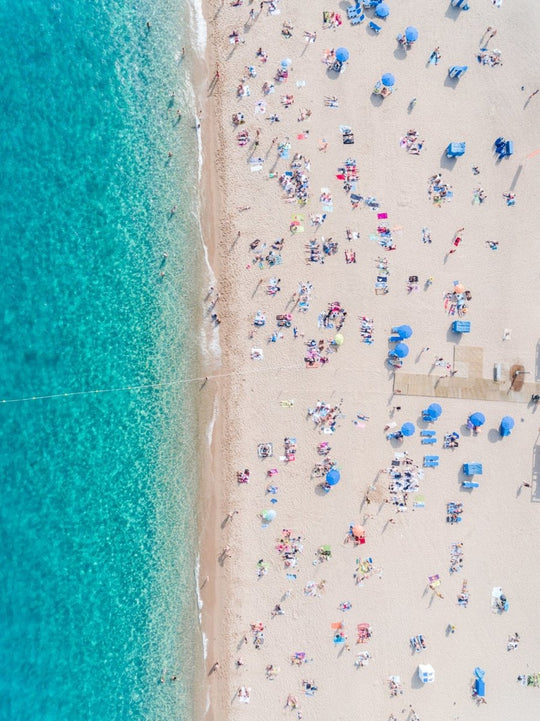 Aerial of blue ocean and people lying on Lloret de Mar beach