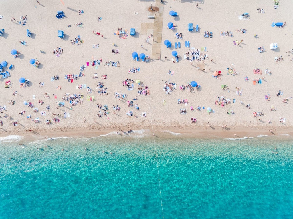Aerial of blue ocean and people lying on Lloret de Mar beach