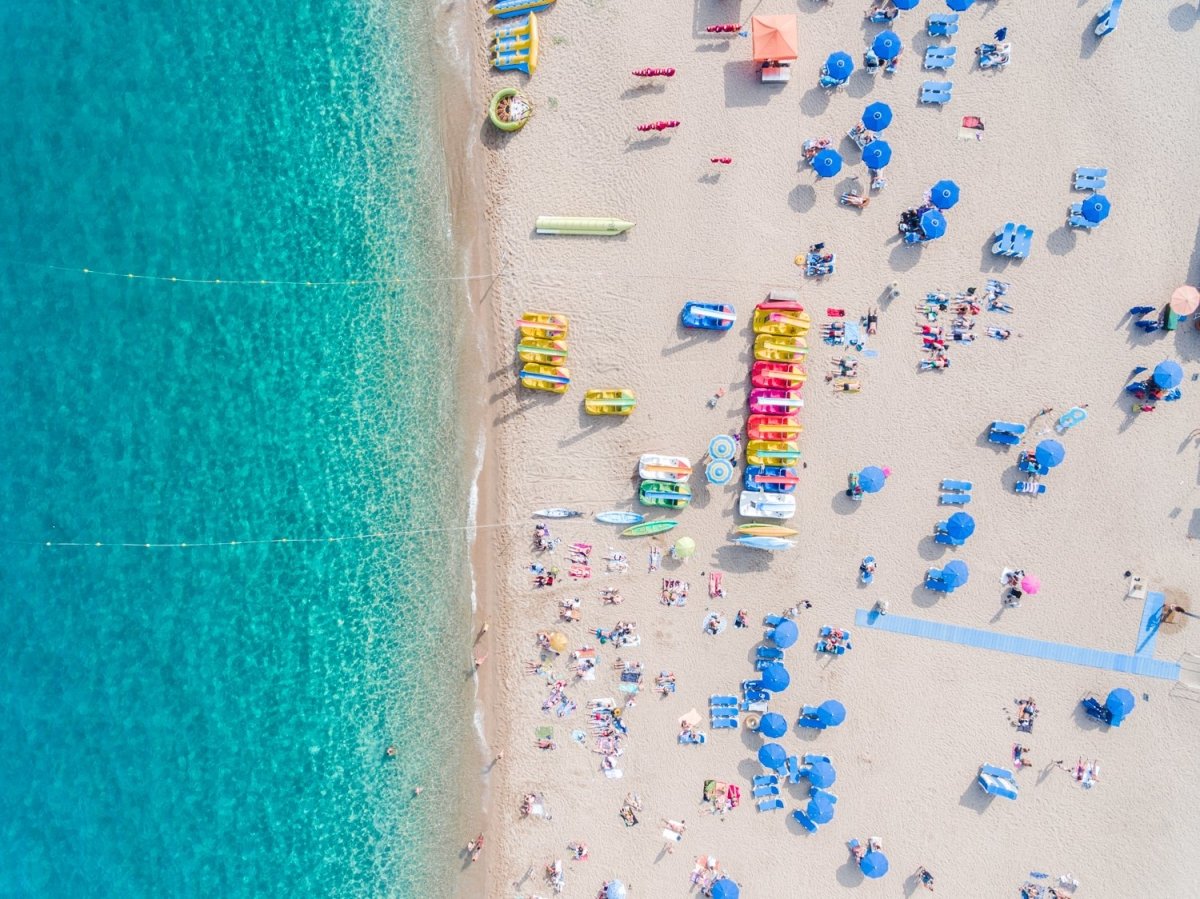 Colorful umbrellas, boats and water seen from air above Lloret de Mar beach