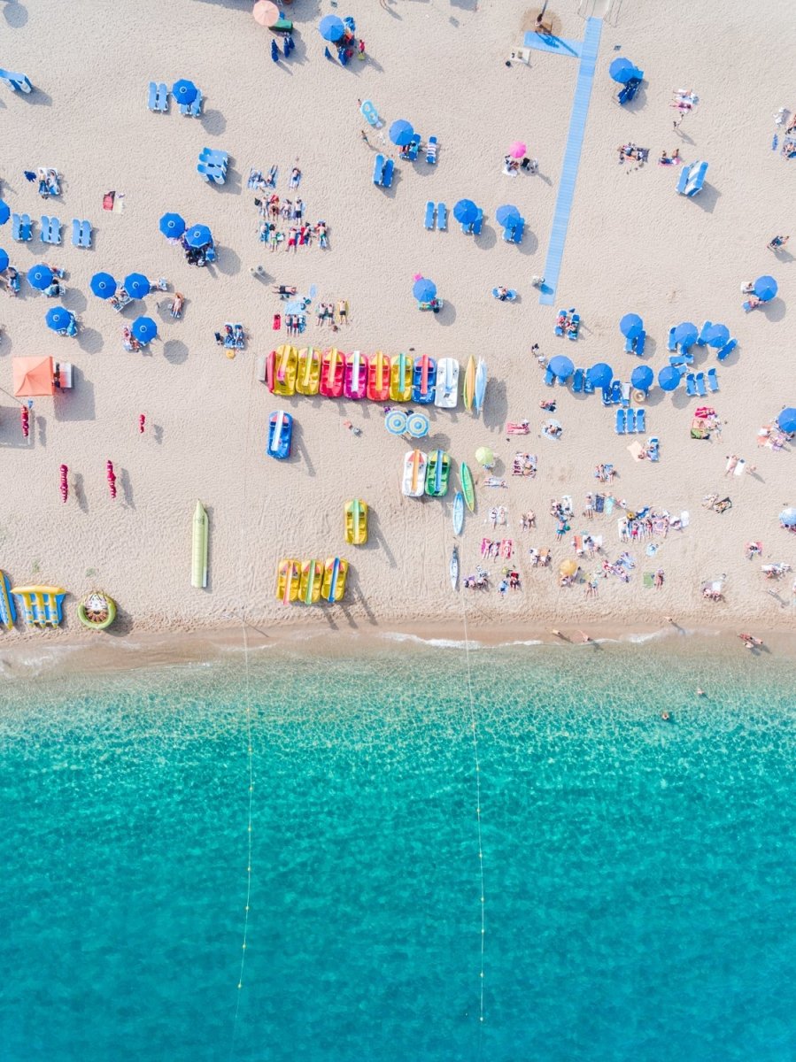 Colorful umbrellas, boats and water seen from air above Lloret de Mar beach