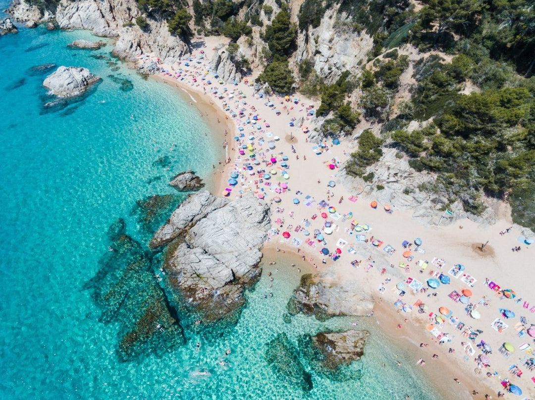 Aerial of bright blue sea, colorful umbrellas and people at Cala sa Boadella beach