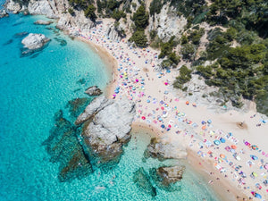 Aerial of bright blue sea, colorful umbrellas and people at Cala sa Boadella beach