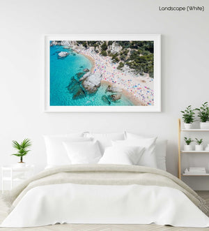 Aerial of bright blue sea, colorful umbrellas and people at Cala sa Boadella beach in a white fine art frame