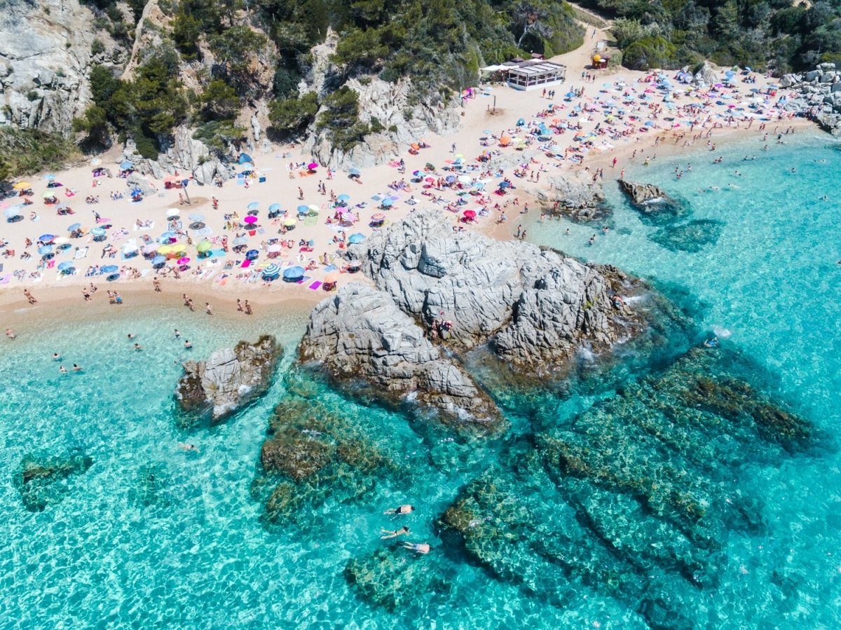 People swimming, snorkeling and tanning along blue water of spanish beach