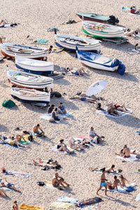 People lying on sand next to boats