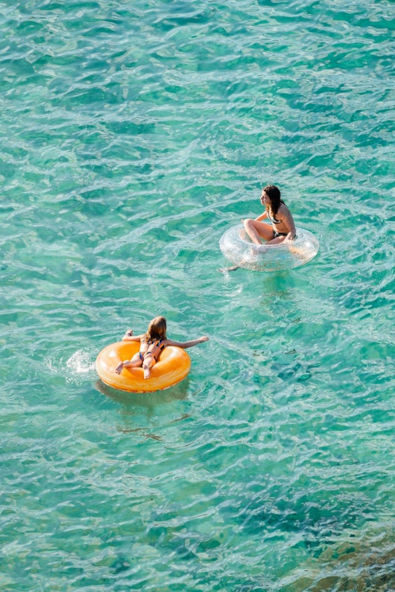 Young girl and woman floating on round lilos in turquoise sea