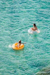 Young girl and woman floating on round lilos in turquoise sea
