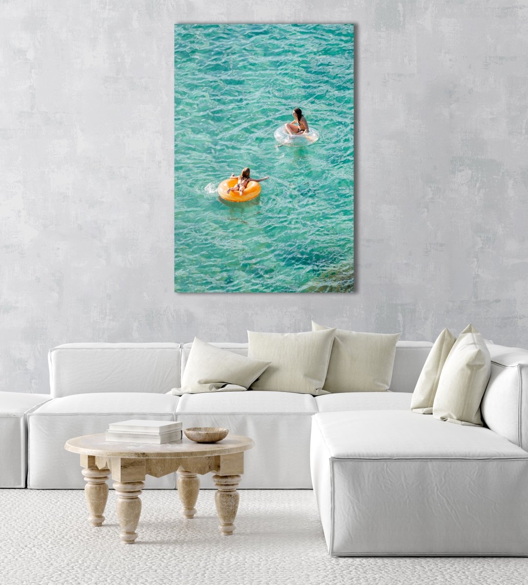 Young girl and woman floating on round lilos in turquoise sea in an acrylic/perspex frame