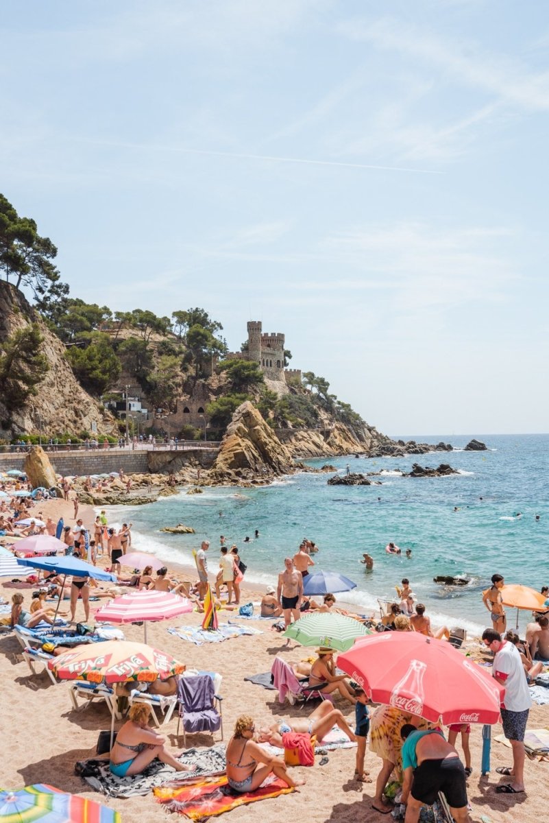 Umbrellas, people on sand and a castle along Costa Brava