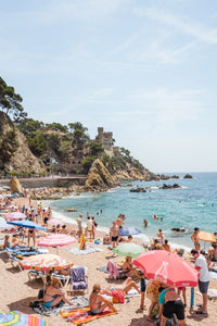 Umbrellas, people on sand and a castle along Costa Brava