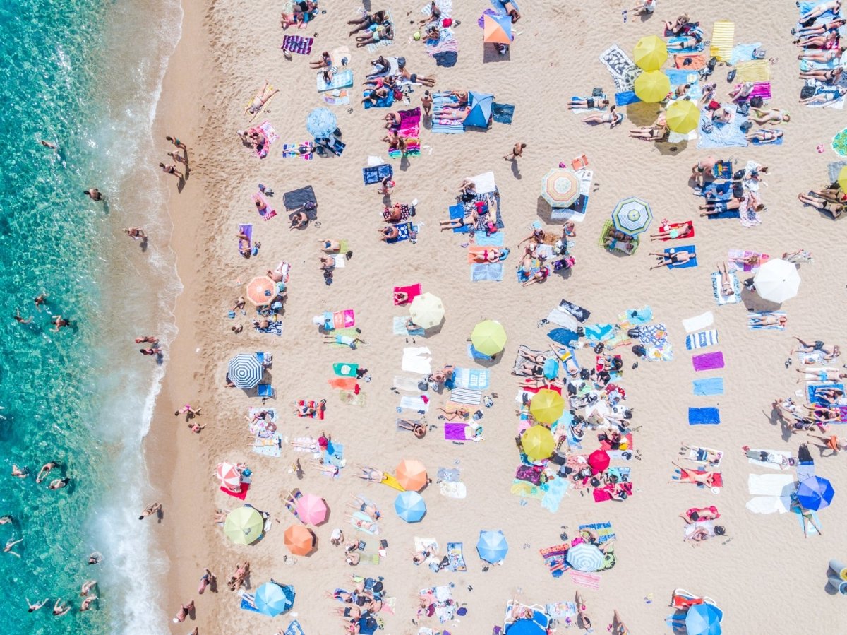 Very crowded Lloret de Mar beach from above with blue water, colorful towels and umbrellas