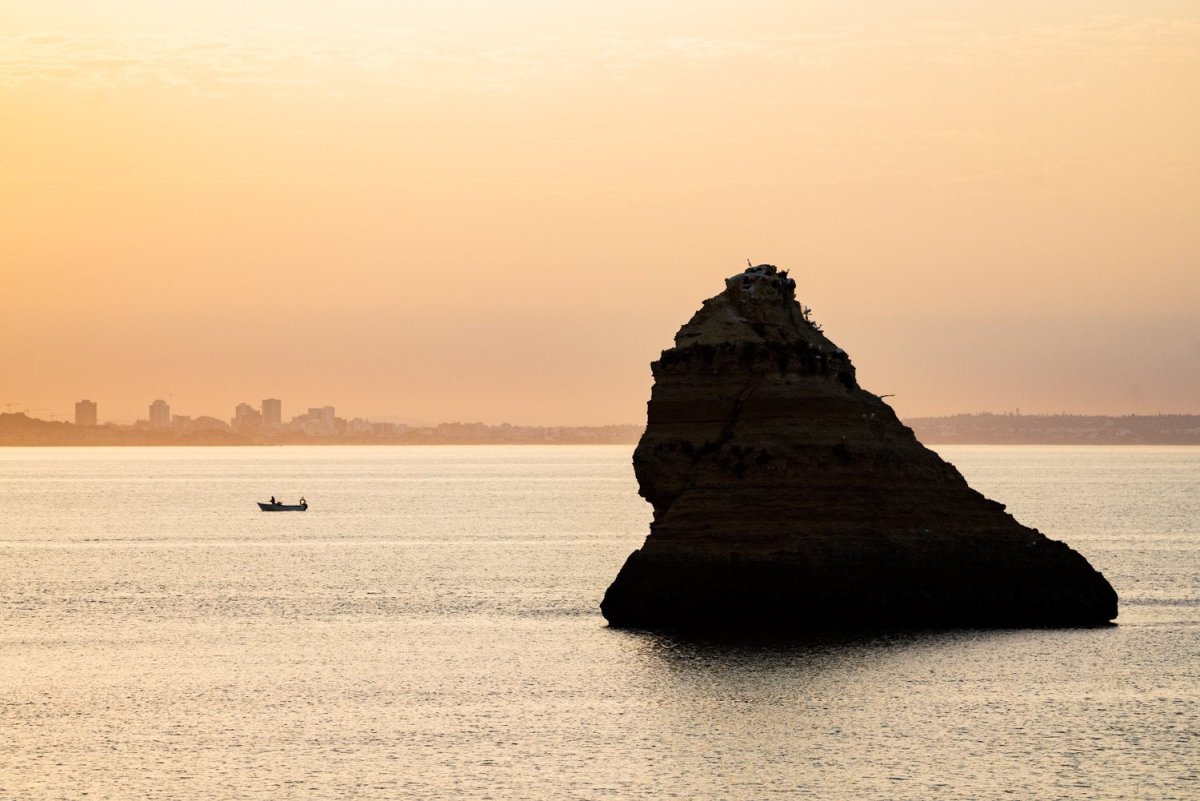 Large boulder and a fishing boat during Lagos sunrise