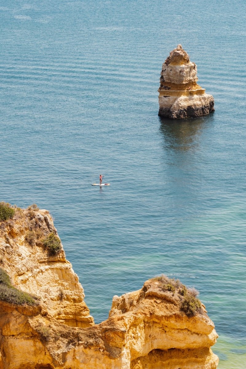 Woman on a SUP in the ocean along Lagos blue water and cliffs