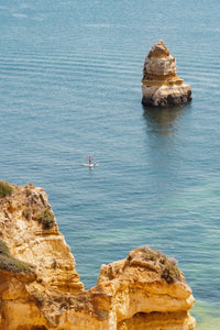 Woman on a SUP in the ocean along Lagos blue water and cliffs