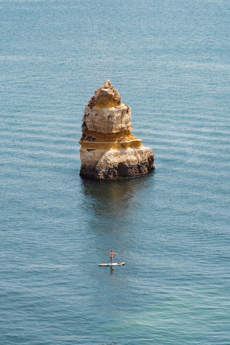 Woman on a SUP paddling near big cliff in Lagos
