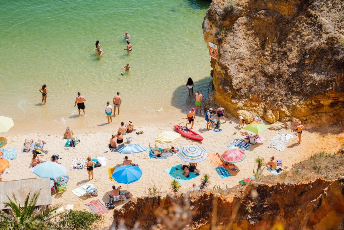 Crowd of people lying with umbrellas and swimming in green sea on Camilo beach