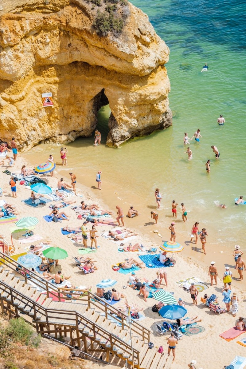 Stairway leading down to people, umbrellas, sand and green water on Camilo beach