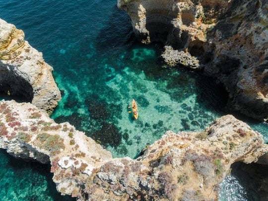 Aerial of two people paddling yellow kayak near Lagos caves in ocean