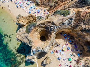 Aerial of a cave tunnel on Camilo Beach in Lagos with people on beach