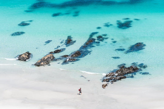 Person walking along crystal clear blue water at beach wall art