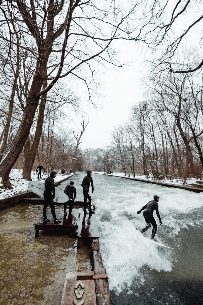 People surfing river wave in the city during snowfall in munich.