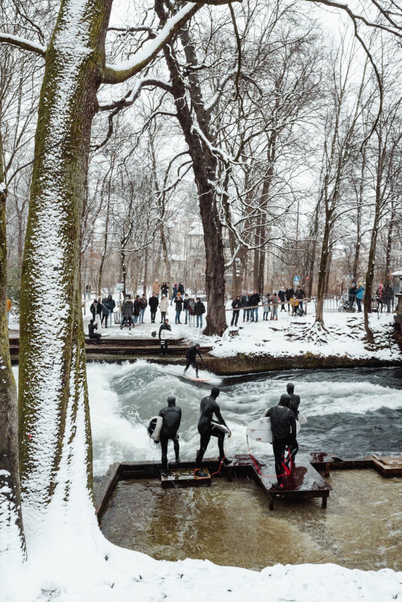 People surfing river wave in the city during snowfall in munich.