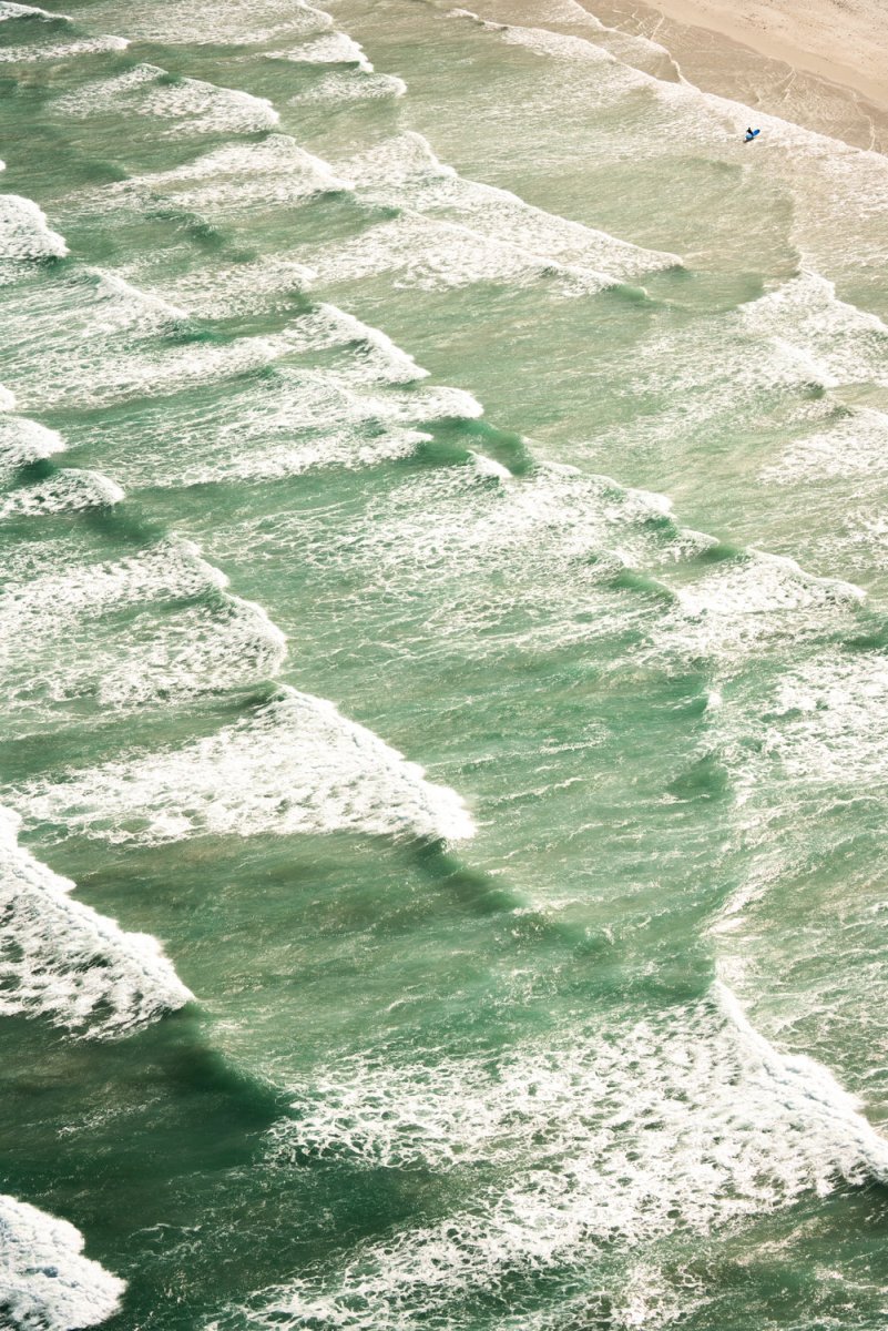 Many waves crashing along Muizenberg beach with a surfer in the corner walking out of the water.