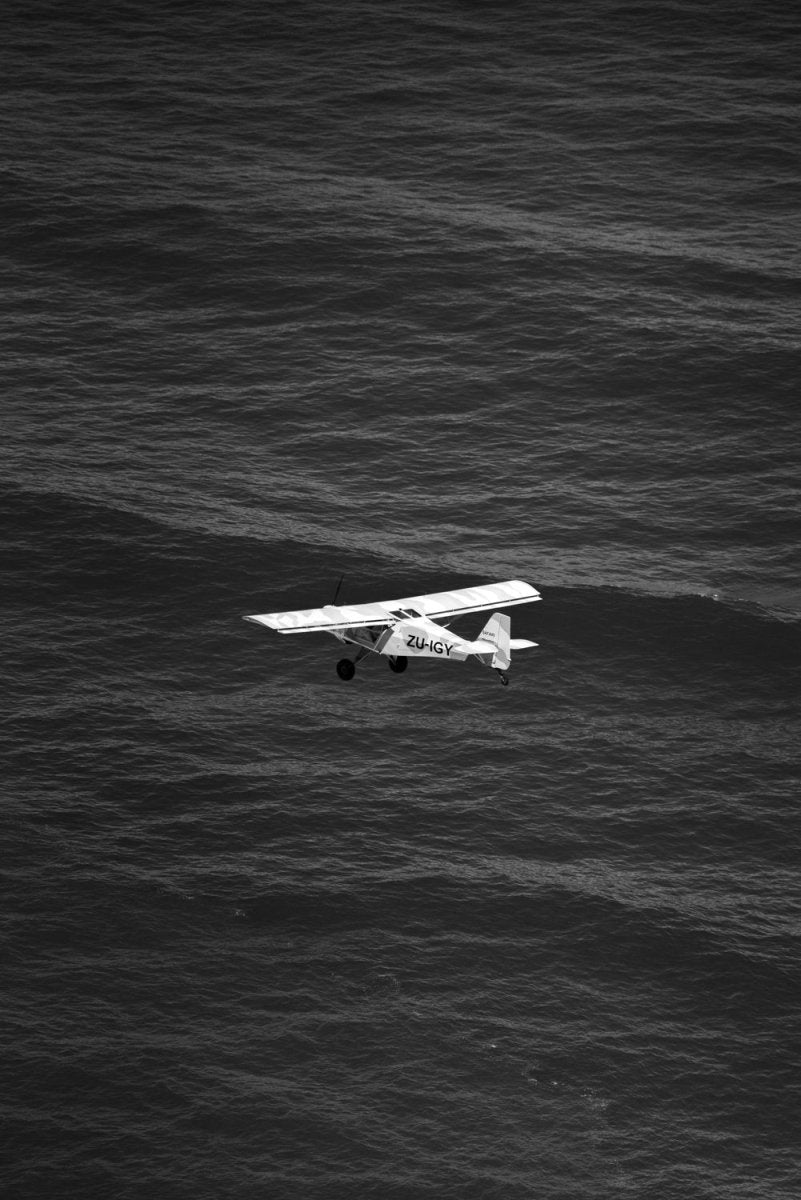 Airplane flying across the ocean at Blouberg Beach in black and white.
