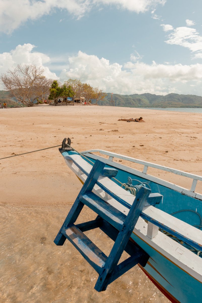 Girl lying on an island in Lombok, Indonesia with blue boat anchored.