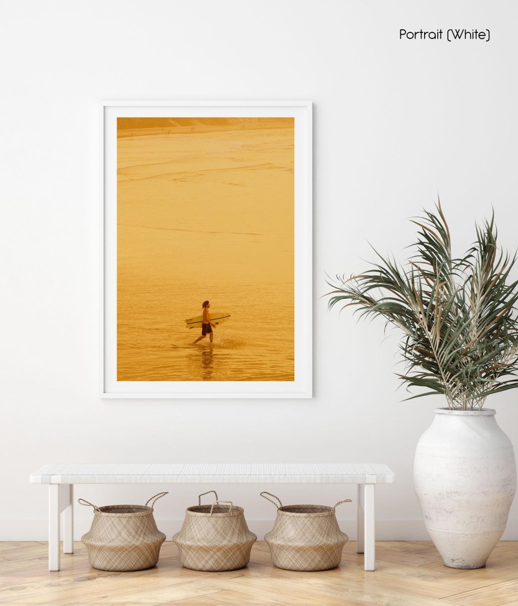 Surfer walking into ocean with orange haze from sunset in byron bay