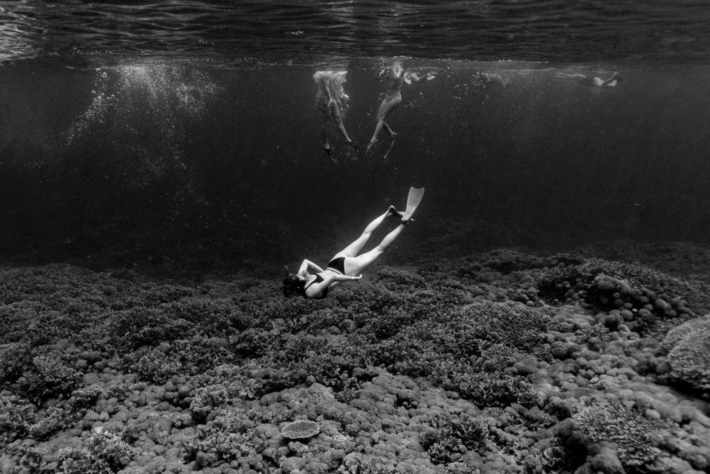 Girl diving underwater along clear coral reef in Bali